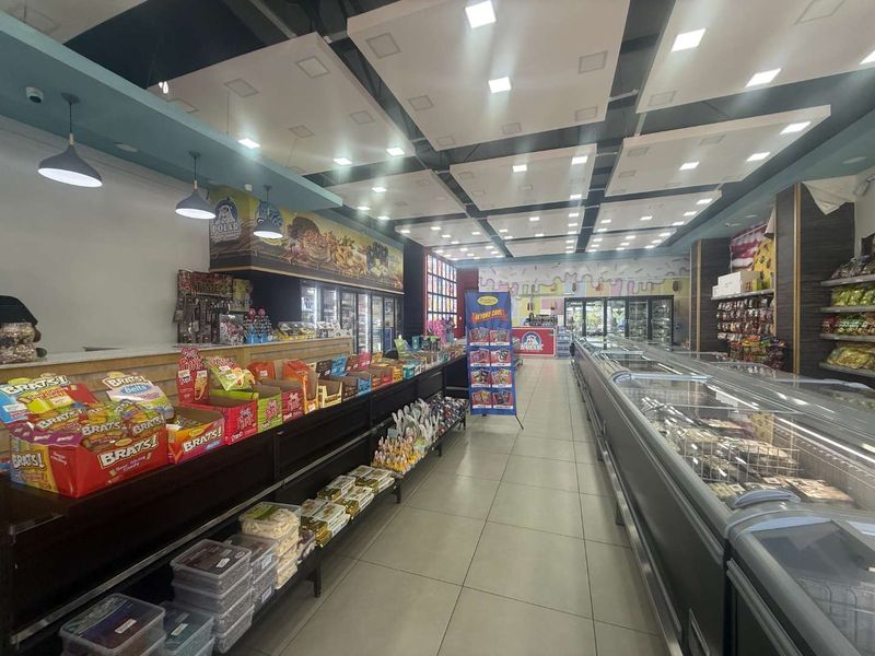 A well-maintained commercial retail space featuring modern suspended ceiling panels, recessed lighting, tiled flooring, and extensive commercial refrigeration units for product display.