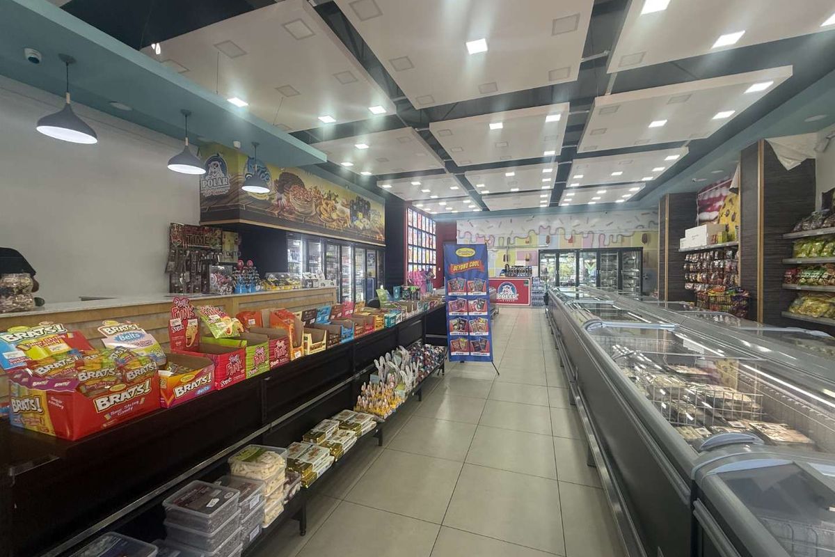 A well-maintained commercial retail space featuring modern suspended ceiling panels, recessed lighting, tiled flooring, and extensive commercial refrigeration units for product display.