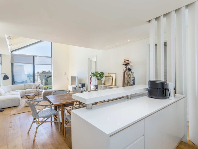 Bright open-plan living and dining area featuring modern kitchen island, timber flooring, and expansive windows with natural light.