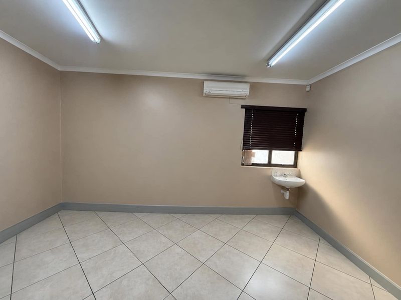 A clean, empty office space featuring tiled flooring, a wall-mounted basin, and an integrated air conditioning unit.