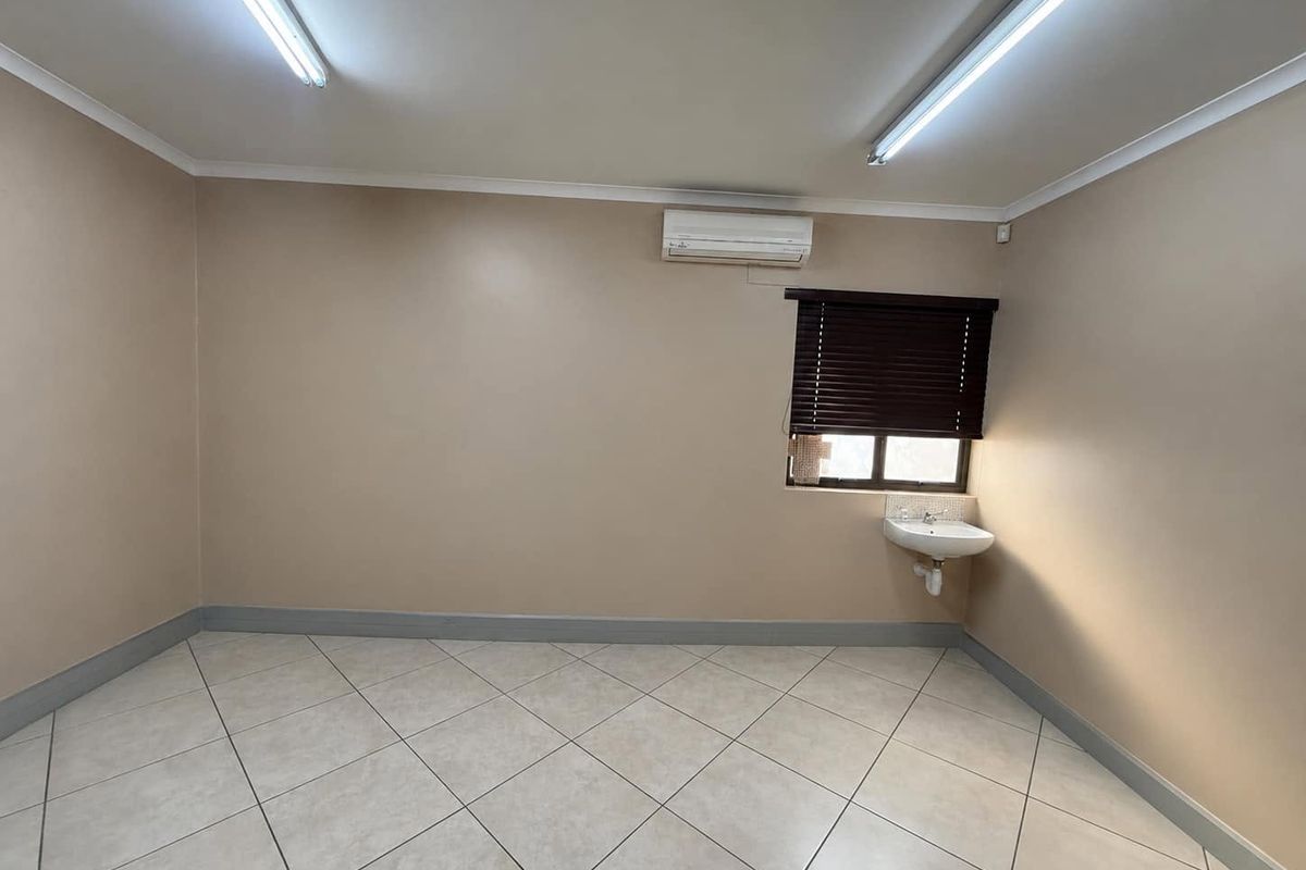 A clean, empty office space featuring tiled flooring, a wall-mounted basin, and an integrated air conditioning unit.