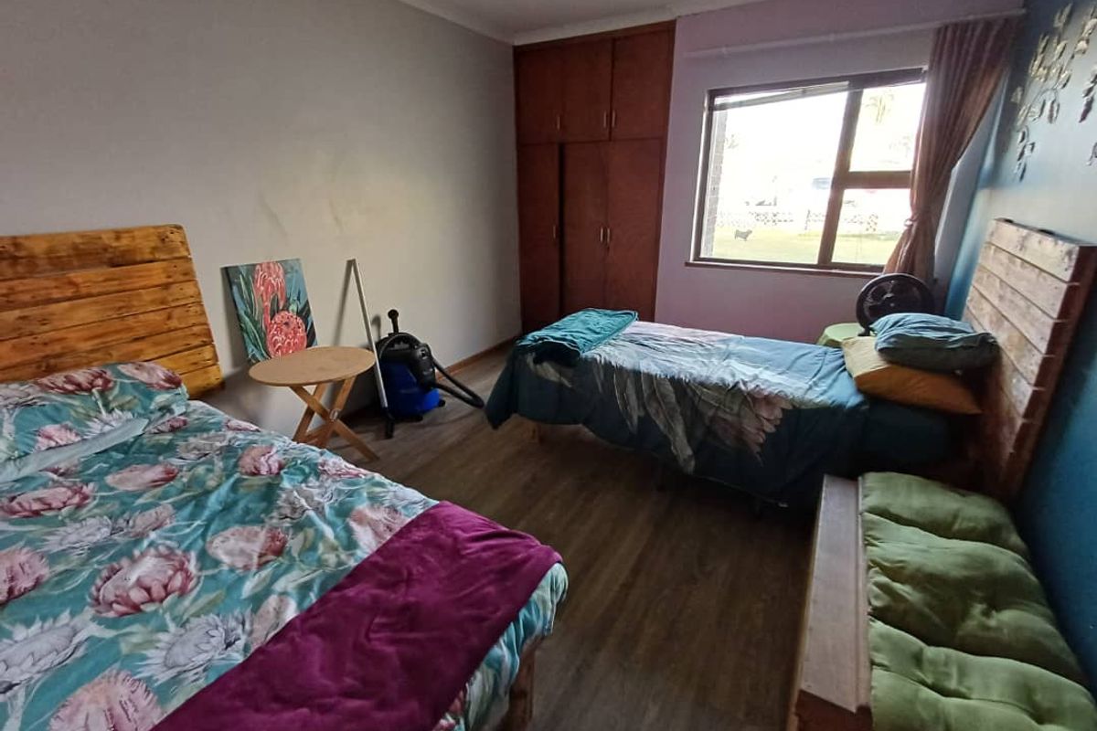 A bedroom featuring built-in wooden cupboards, laminate flooring, and a large window providing natural light.