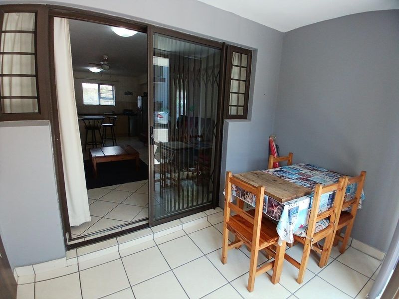 A covered patio area featuring tiled flooring and a sliding glass door with a security gate, providing direct access to the interior living space.