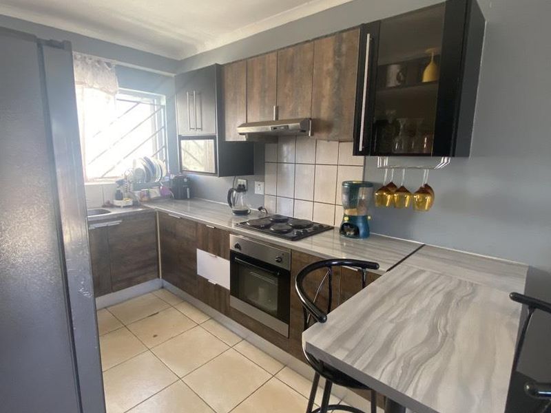 Compact kitchen featuring wood-look cabinetry, laminate countertops, built-in oven and hob, tiled backsplash, and a small breakfast bar area.