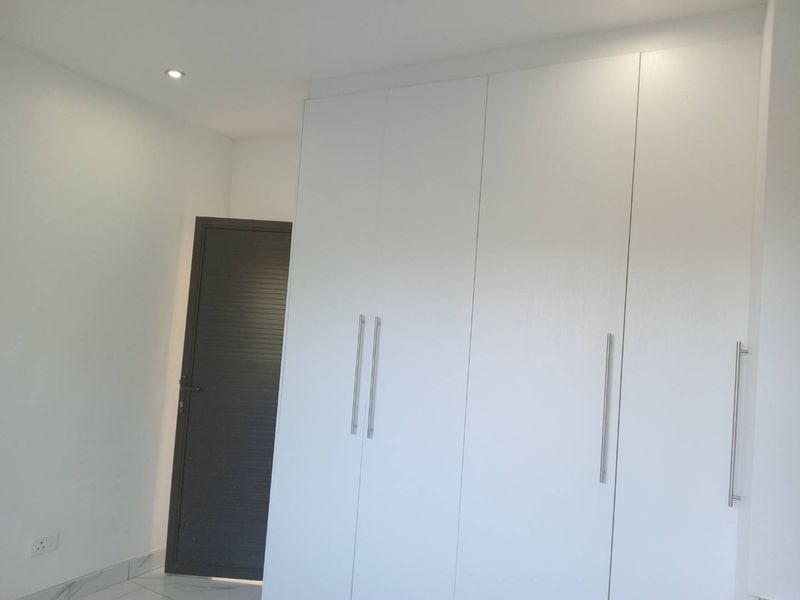 A clean, modern bedroom featuring white built-in cupboards, tiled flooring, and recessed downlighting, offering a bright and neutral space ready for personalization.