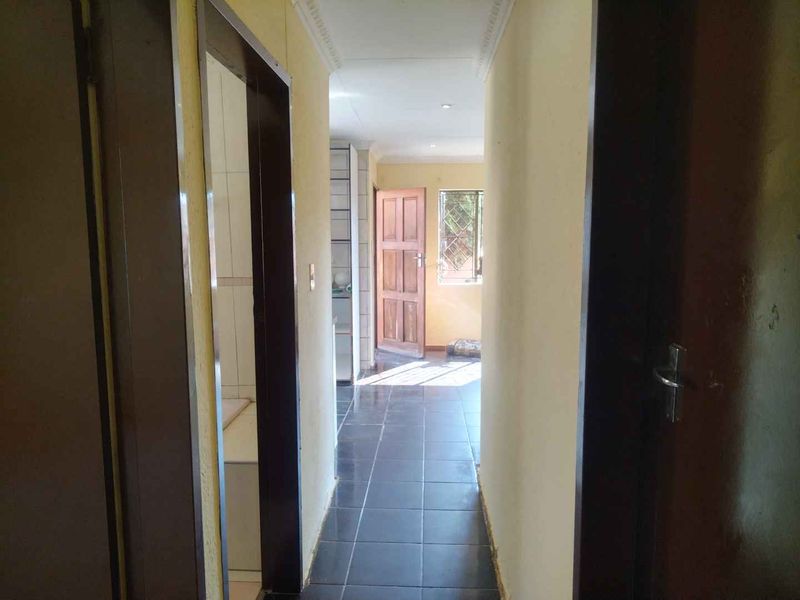A functional hallway featuring dark tiled flooring, coved ceilings, and recessed lighting, providing access to adjacent rooms within the property.