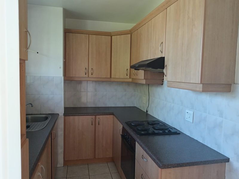 A functional kitchen featuring light wood-finish cabinetry, dark laminate countertops, built-in oven, electric hob, extractor fan, and tiled splashbacks.