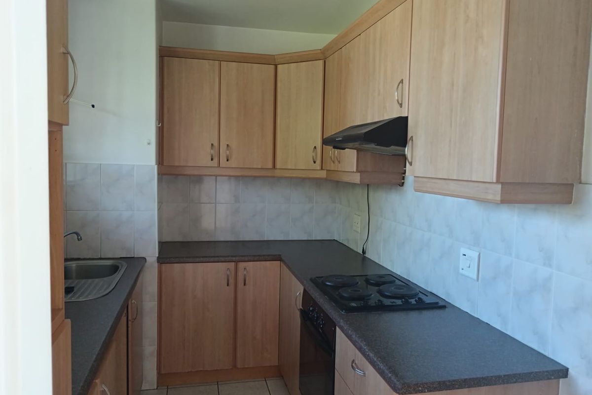 A functional kitchen featuring light wood-finish cabinetry, dark laminate countertops, built-in oven, electric hob, extractor fan, and tiled splashbacks.