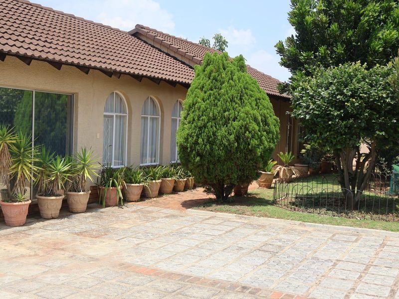 A well-maintained rear exterior view featuring a paved patio area, arched windows, and sliding glass doors leading into the home.