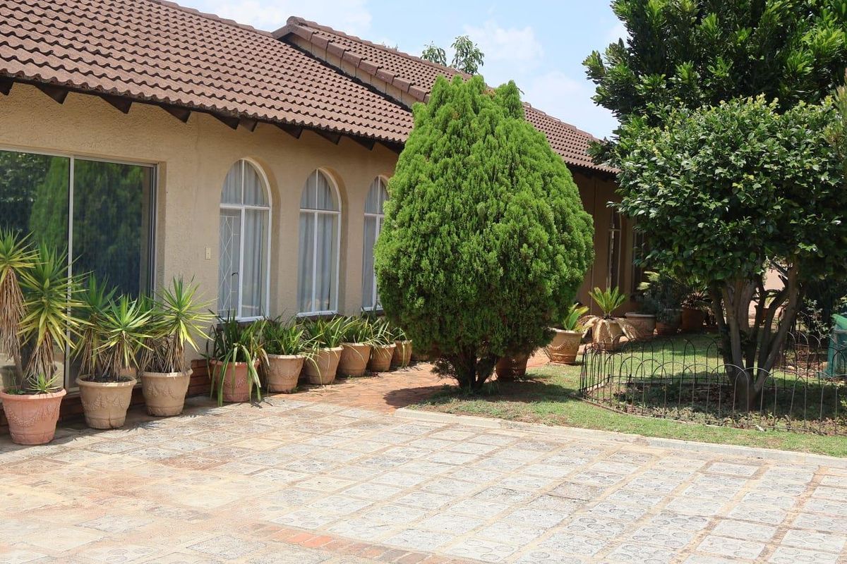 A well-maintained rear exterior view featuring a paved patio area, arched windows, and sliding glass doors leading into the home.
