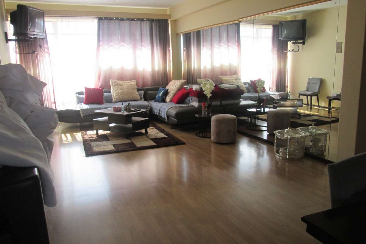 Spacious living room featuring laminate wood flooring and a large wall-mounted mirror, creating an open and bright atmosphere.