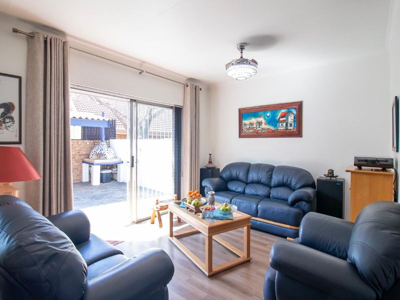 A bright living room featuring laminate flooring, a ceiling fan, and a sliding glass door providing direct access to the outdoor patio area.