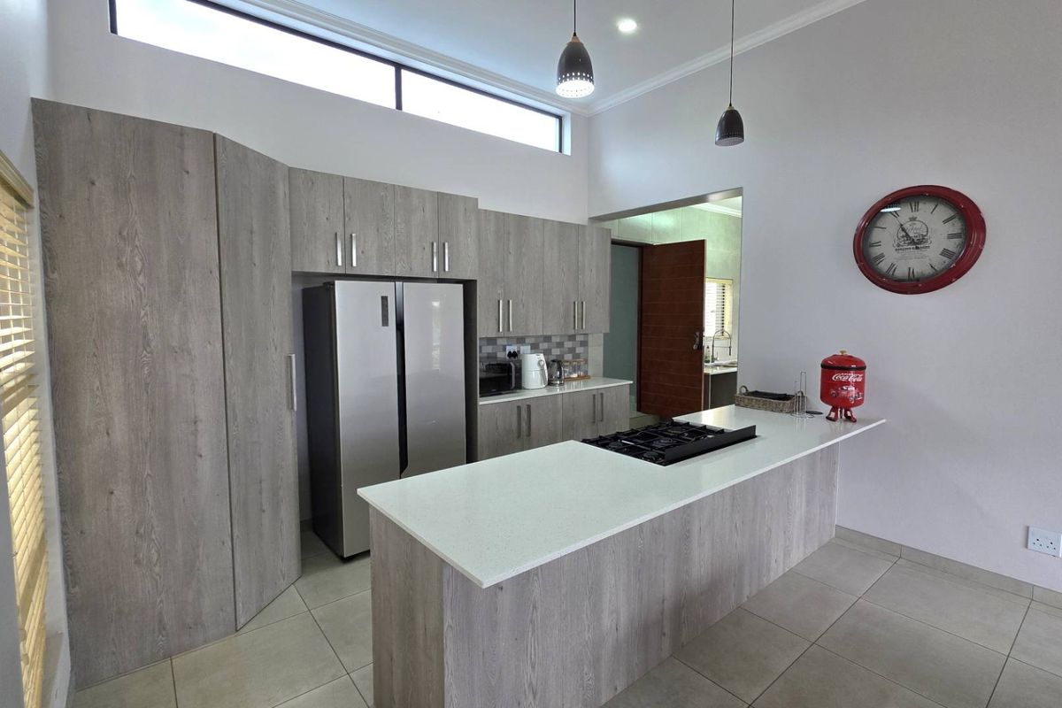 Modern kitchen featuring light wood-grain cabinetry, a central island with a built-in gas hob, stone countertops, and high-level clerestory windows for natural light.