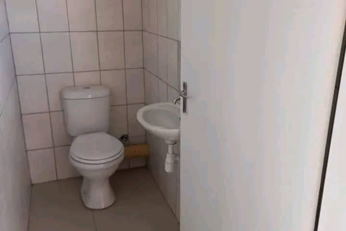 A functional small restroom featuring a white ceramic toilet and a wall-mounted basin with tiled walls and flooring.