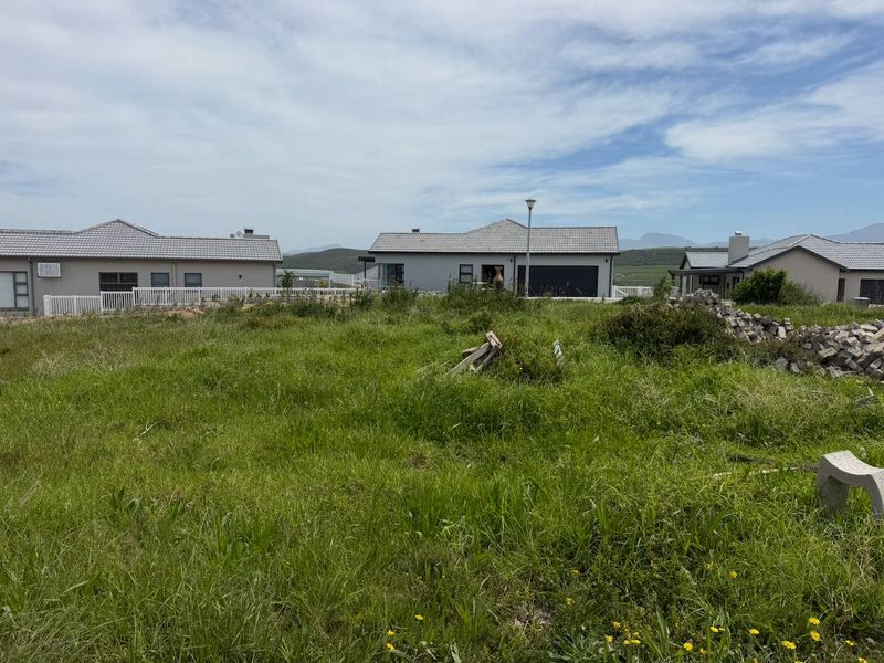 A view of a vacant residential plot situated within an established neighborhood, featuring surrounding modern homes and mountain views in the distance.