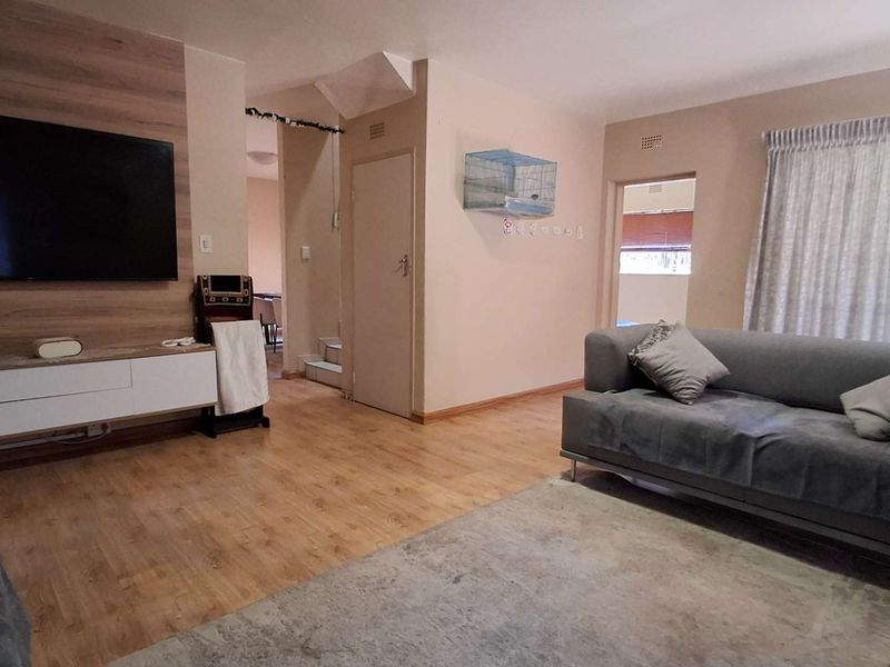 A living room featuring laminate flooring and a built-in media wall unit, providing a functional space with access to adjacent areas.