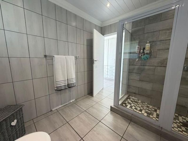 Modern bathroom featuring a walk-in shower with mosaic floor tiling, neutral wall tiles, and a tongue and groove ceiling.