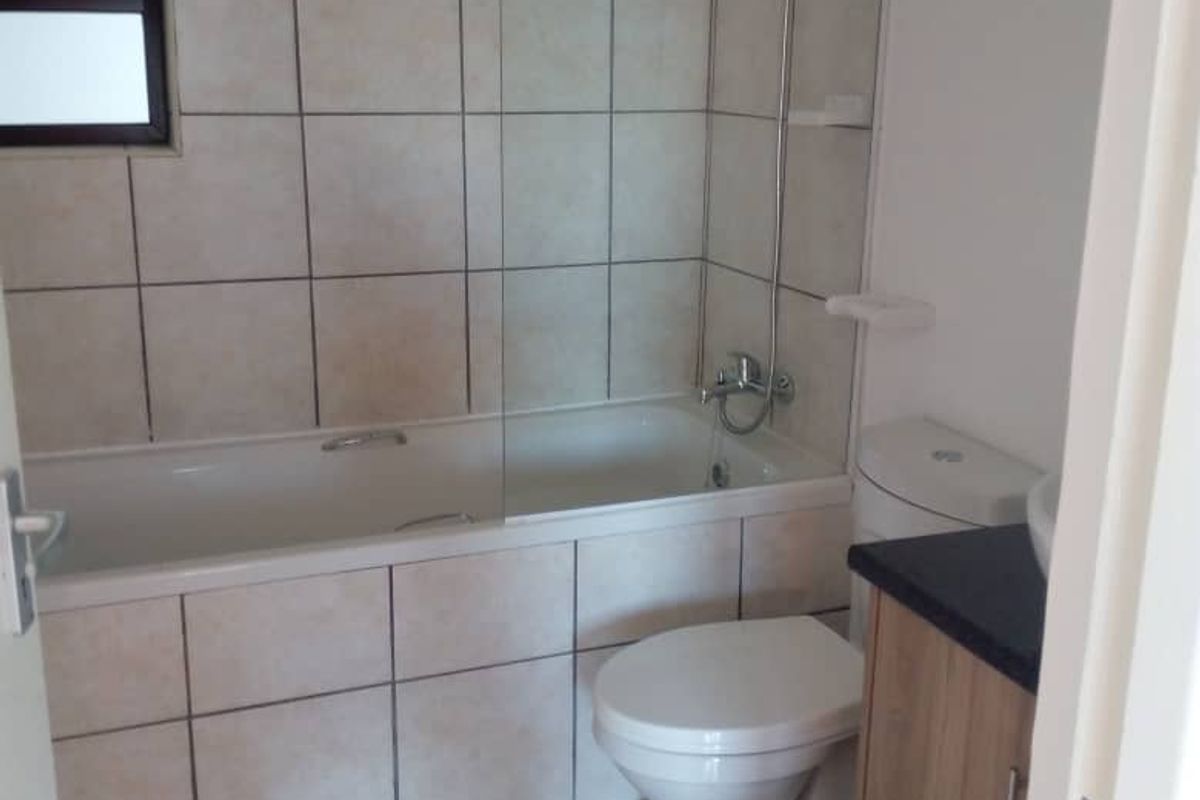 A functional bathroom featuring a bathtub with a glass shower screen, a toilet, and a vanity cabinet with a countertop.