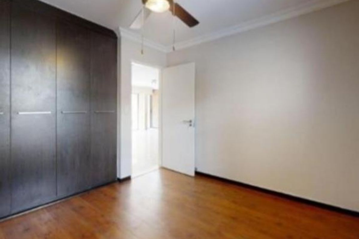 A bright, empty bedroom featuring dark wood-finish built-in cupboards, warm laminate flooring, and a ceiling fan.