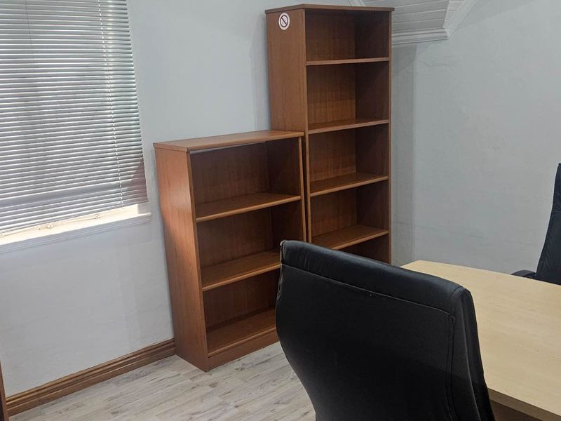 A functional office space featuring wood-look flooring, dual windows with fitted blinds, and neutral wall finishes.