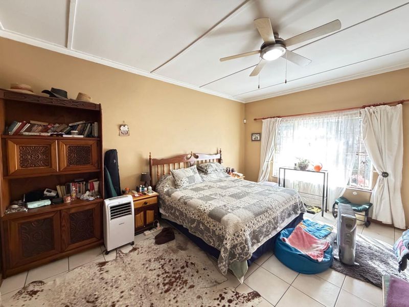 A spacious bedroom featuring tiled flooring and a ceiling fan, offering a functional layout with natural light from the window.