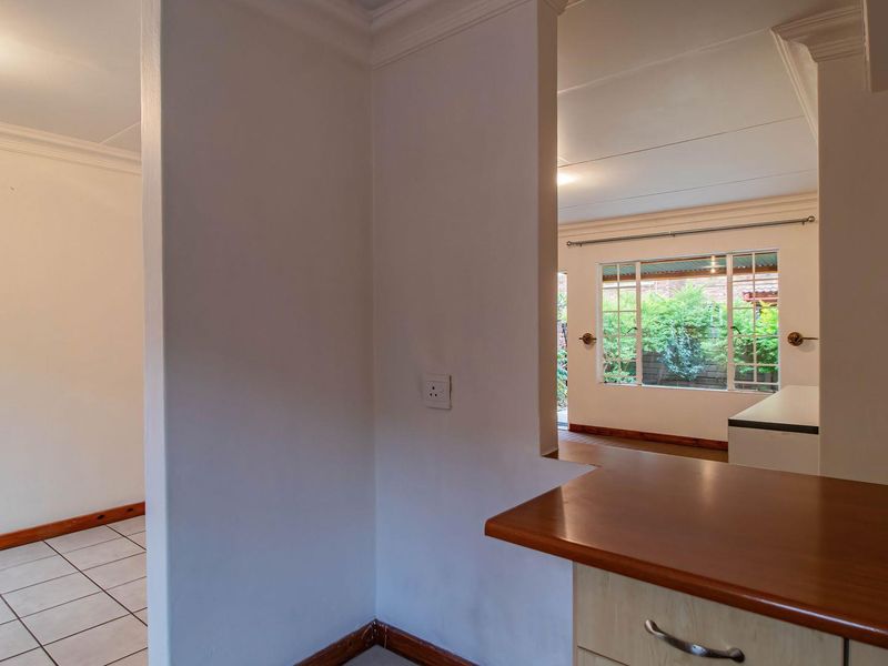 An open-plan living area featuring tiled floors, built-in cabinetry with a wooden countertop, and views through a window to the garden.