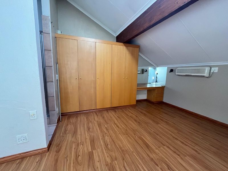 Spacious bedroom featuring vaulted ceilings, exposed timber beams, laminate flooring, built-in cupboards, and a dedicated vanity area with air conditioning.