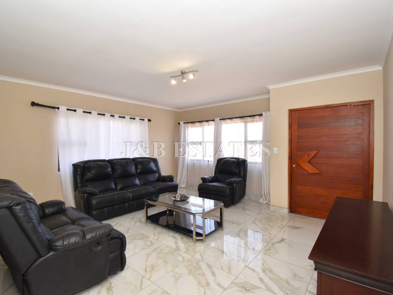 A well-maintained living room featuring polished marble-look floor tiles, neutral wall tones, and a solid timber entrance door.