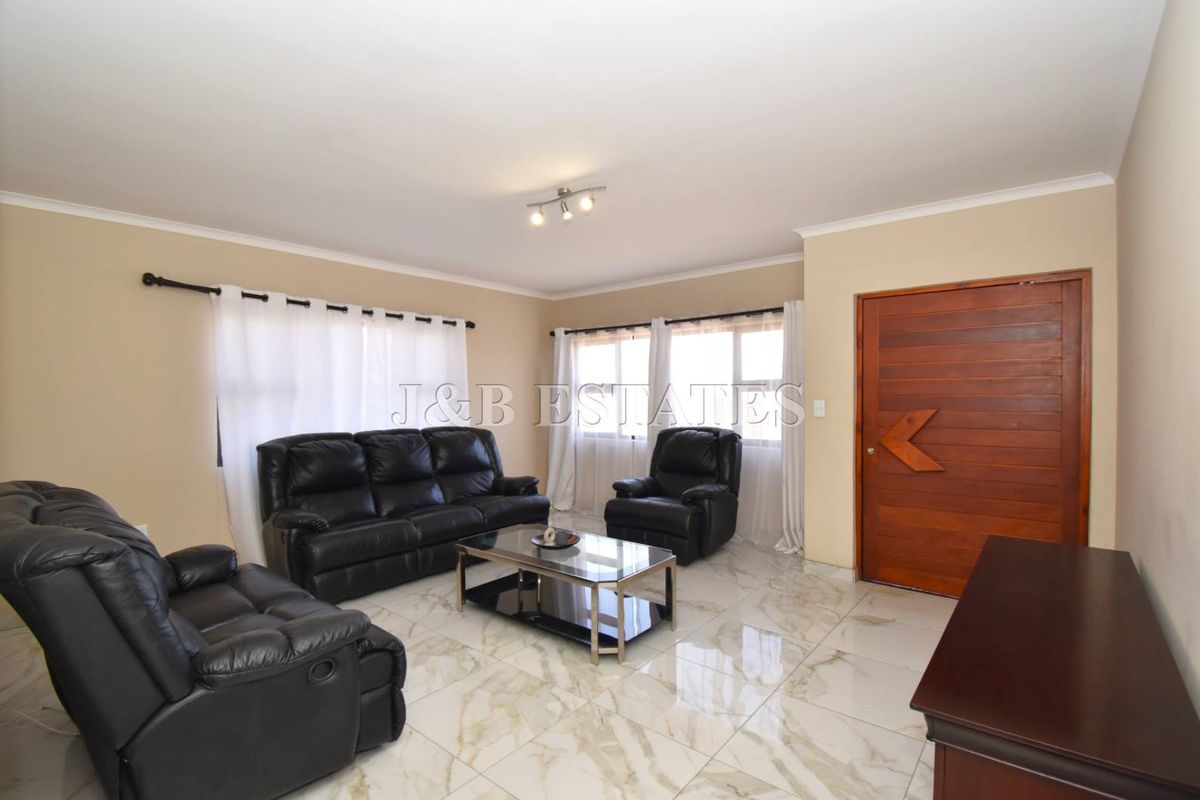 A well-maintained living room featuring polished marble-look floor tiles, neutral wall tones, and a solid timber entrance door.