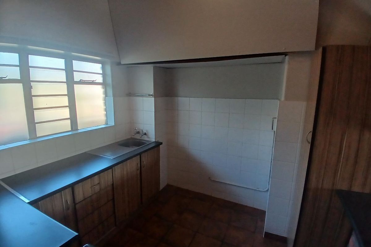 A functional kitchen area featuring wood-finish cabinetry, a stainless steel sink, and tiled splashbacks, offering a practical layout for culinary tasks.