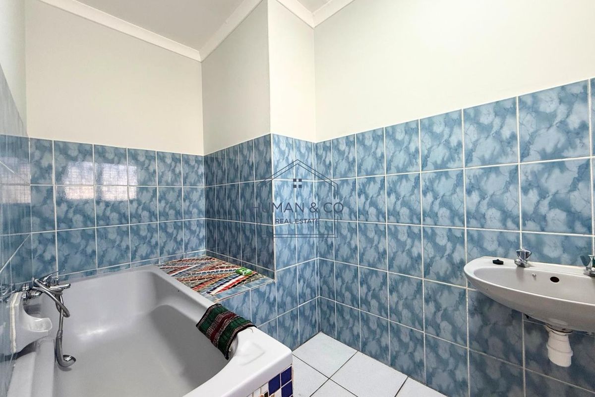 A dated bathroom featuring blue patterned wall tiles, a standard bathtub with handheld shower mixer, and a wall-mounted basin.