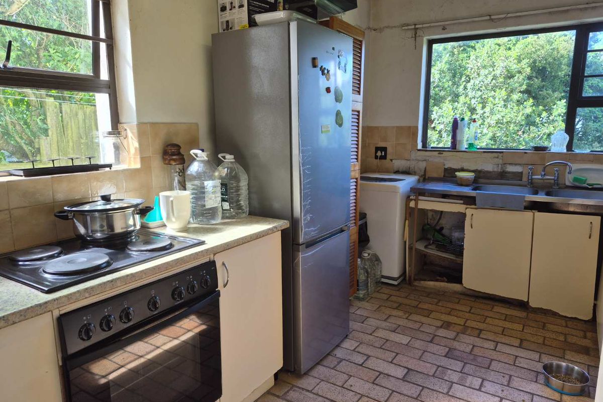 A functional kitchen space featuring a built-in oven, electric hob, and stainless steel sink, requiring cosmetic updates and cabinetry repairs to improve its overall condition.