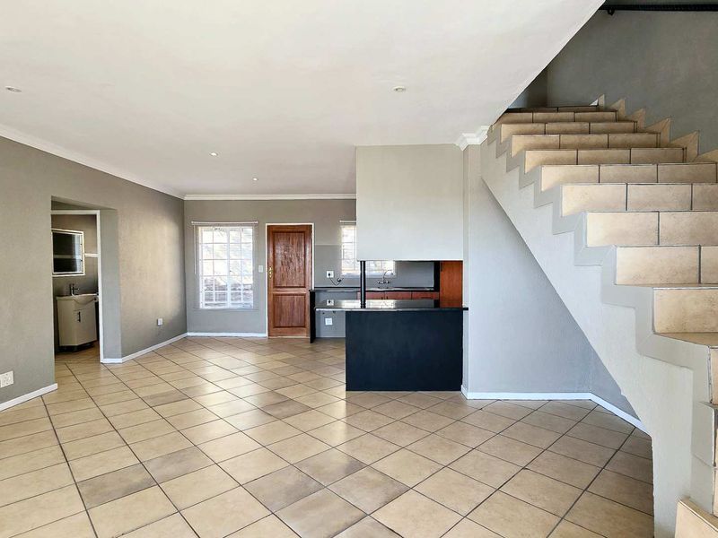 Spacious open-plan living area featuring tiled flooring, a built-in staircase, and a functional kitchen layout with neutral wall finishes.