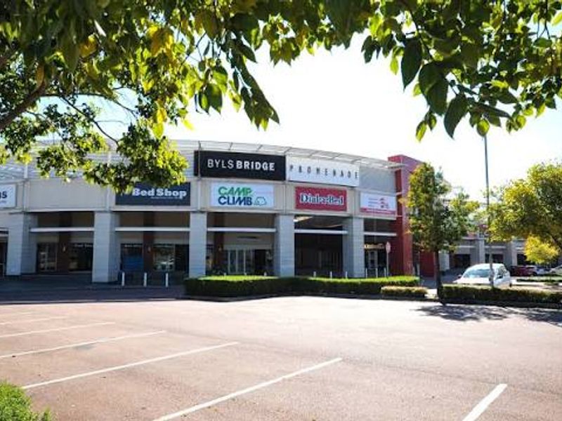 Front exterior view of the Byls Bridge Promenade commercial office and retail complex featuring paved parking and multiple storefronts.