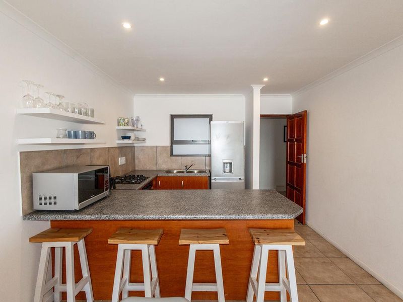 Compact kitchen featuring wooden cabinetry, stone-look countertops, a gas hob, and integrated shelving, providing a functional and efficient cooking space.