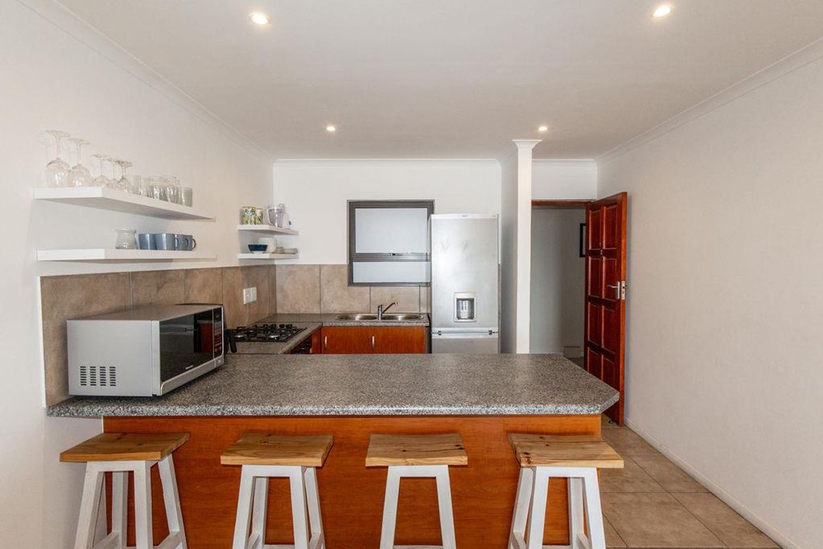Compact kitchen featuring wooden cabinetry, stone-look countertops, a gas hob, and integrated shelving, providing a functional and efficient cooking space.