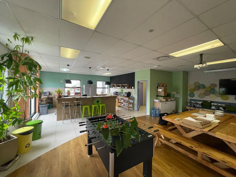 Open-plan office breakout area featuring a kitchenette with a breakfast bar, mixed flooring, and a suspended ceiling with integrated lighting.