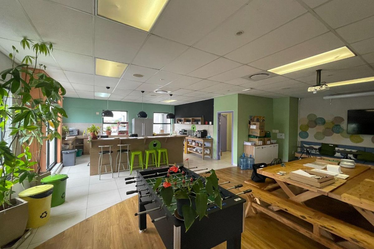 Open-plan office breakout area featuring a kitchenette with a breakfast bar, mixed flooring, and a suspended ceiling with integrated lighting.