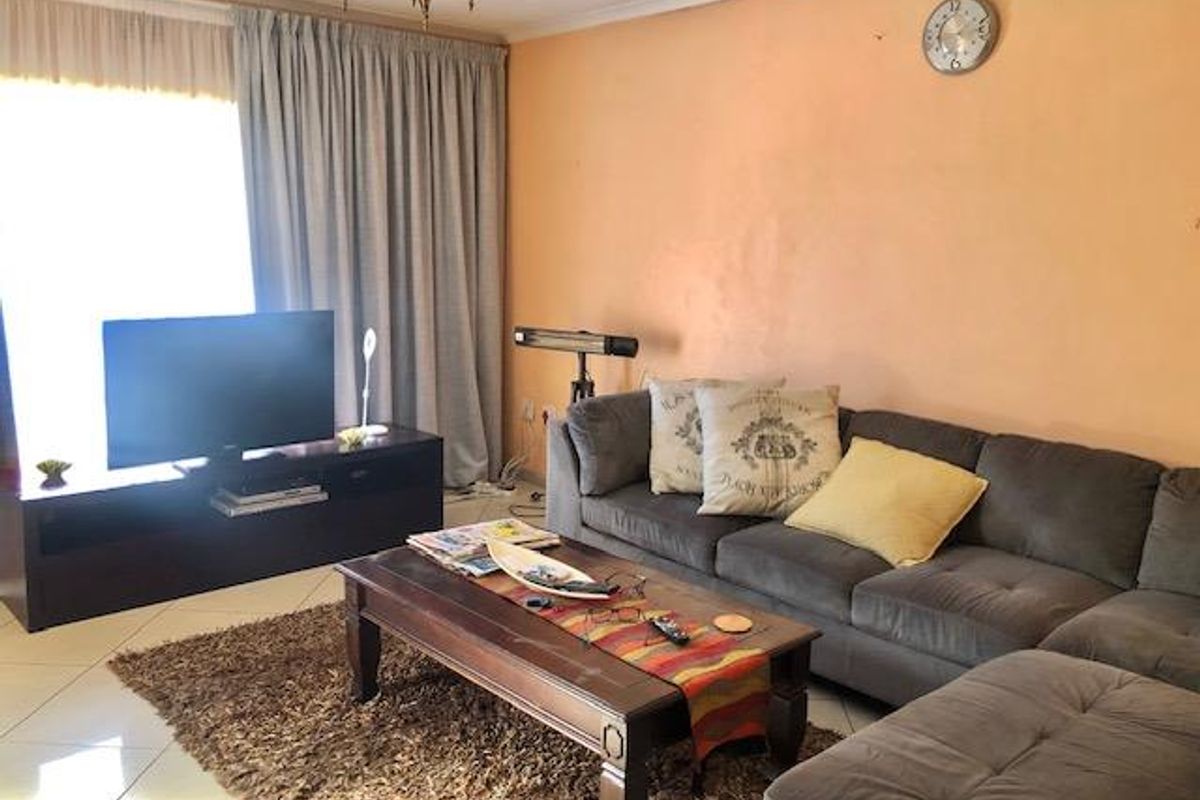 A comfortable living room featuring tiled flooring, large window with curtains, and neutral wall finishes, providing a functional space for relaxation.