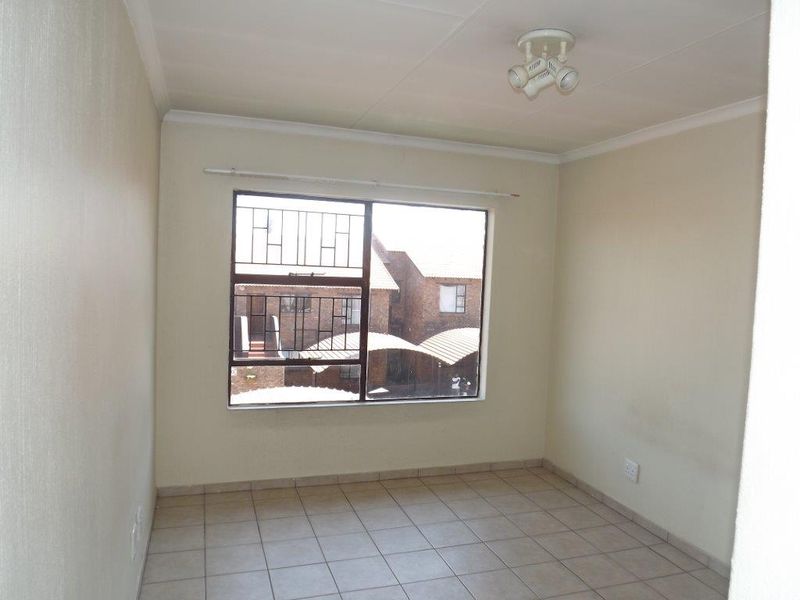 An empty bedroom featuring neutral tiled flooring, security bars on the window, and a ceiling-mounted spotlight fixture.