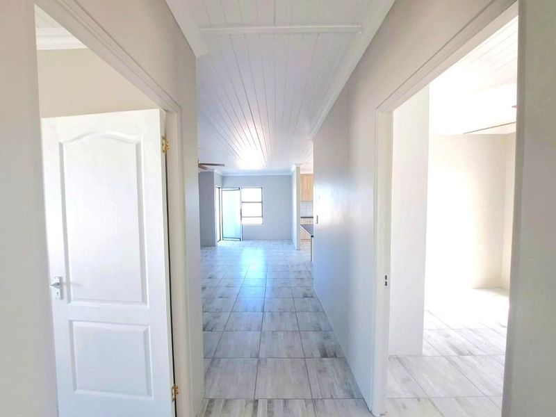 A bright, neutral hallway featuring tiled flooring and a tongue and groove ceiling, providing access to multiple rooms within the home.