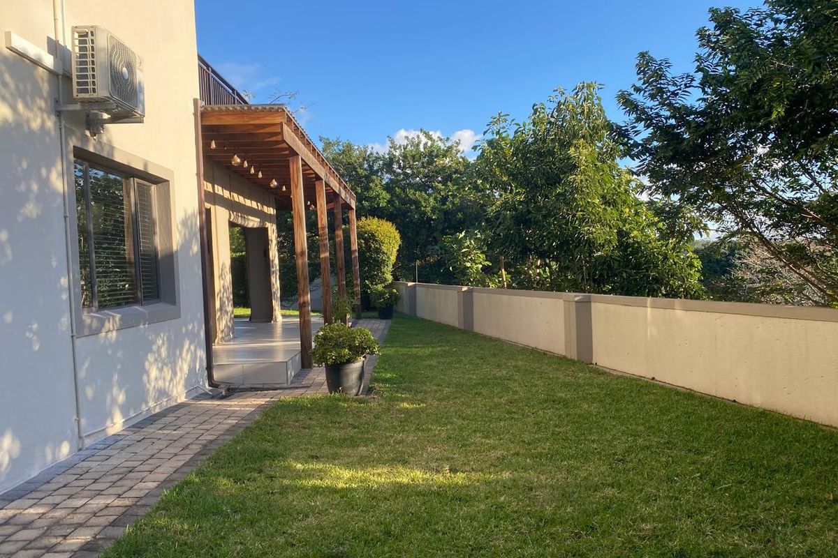 A well-maintained rear garden featuring a paved walkway, a timber pergola structure, and a solid boundary wall, providing a private outdoor space.