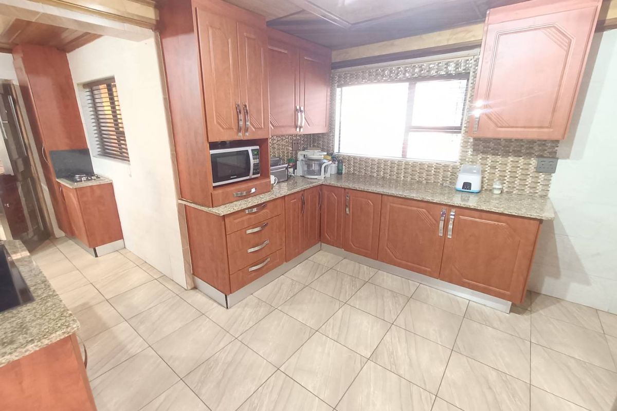A functional kitchen featuring warm-toned wooden cabinetry, granite countertops, mosaic tile backsplash, and tiled flooring with a distinct timber-paneled ceiling.