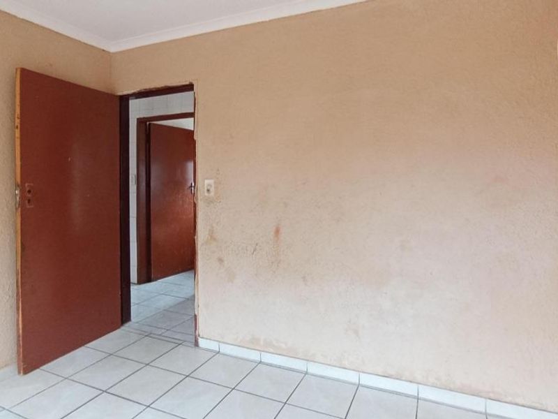 An empty bedroom featuring tiled flooring and plain walls, requiring cosmetic updates and painting to improve its overall condition.