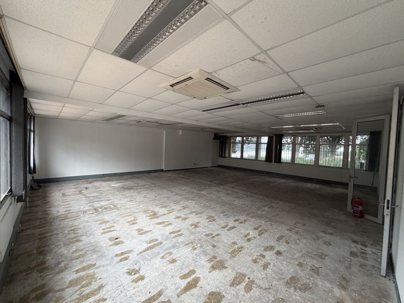Spacious open-plan office area featuring a suspended ceiling with integrated lighting, air conditioning, and large windows with security bars.