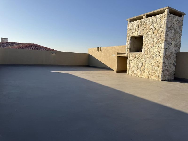 A spacious, open-air rooftop terrace featuring a stone chimney structure and clean, waterproofed flooring, offering a versatile outdoor entertainment space.