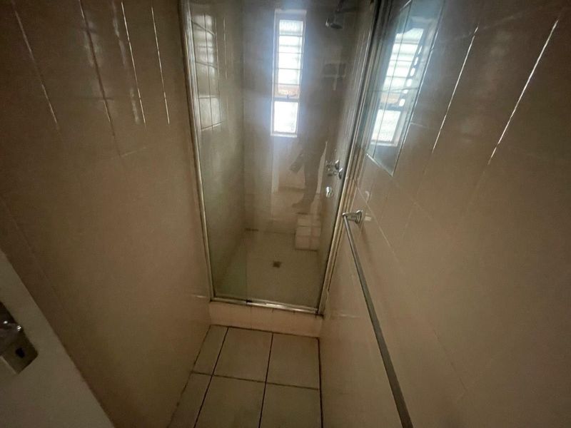 A compact bathroom featuring a shower enclosure with tiled walls and flooring, requiring cosmetic updates to modernize the space.