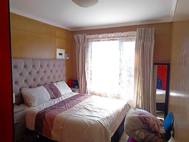 A bedroom featuring tiled flooring and a wall-mounted electrical distribution board, with natural light entering through a large window.