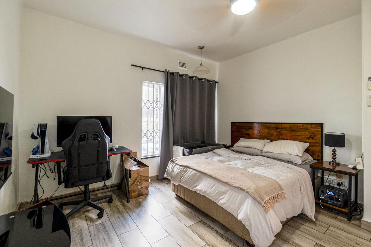 A functional bedroom featuring wood-look tiled flooring, a window with security bars, and a ceiling-mounted light fixture.