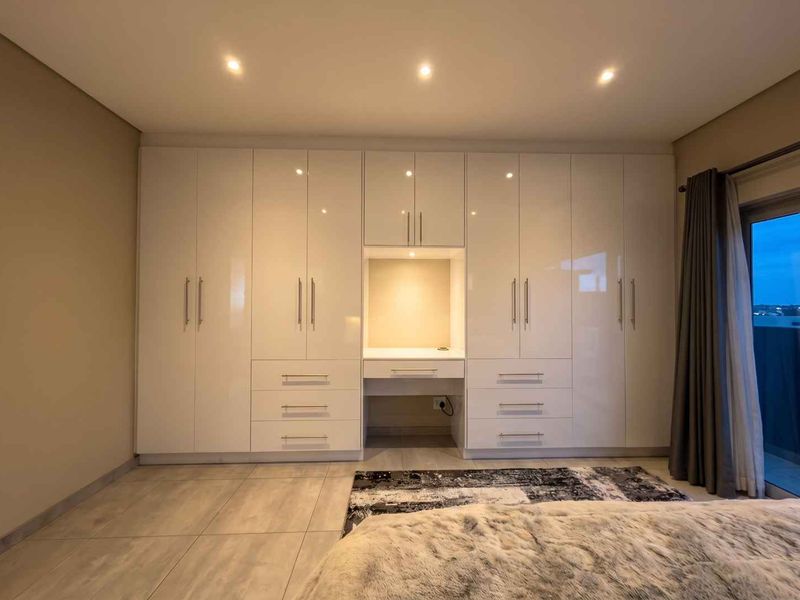 Modern bedroom featuring extensive high-gloss built-in cabinetry with an integrated vanity desk, recessed lighting, and neutral tiled flooring.